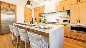 Una cocina moderna con armarios de madera, electrodomésticos de acero inoxidable, una isla central con taburetes y luminarias colgantes.