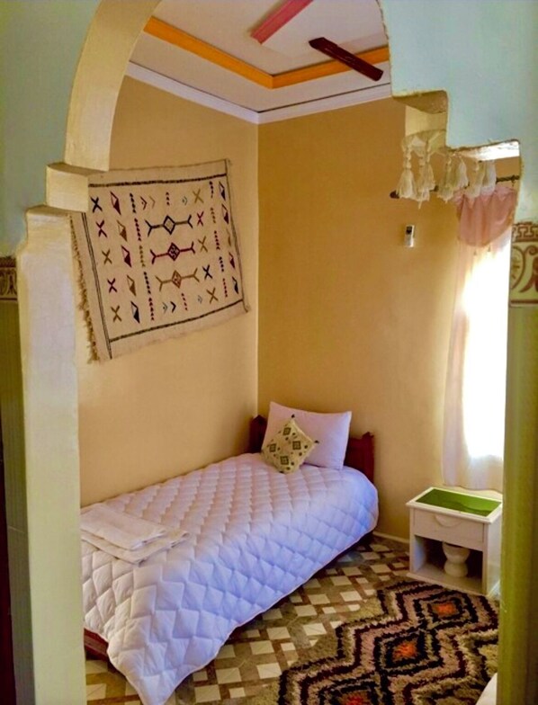 A small, cozy bedroom with a single bed, a patterned rug, and a wall hanging.