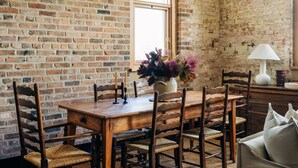 A rustic dining area with a wooden table and chairs, a vase with flowers, and a lamp on a side table. - The Rox Hobart (Hobart)