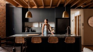 A modern kitchen with dark cabinetry, a central island with bar stools, and pendant lighting. - The Rox Hobart (Hobart)
