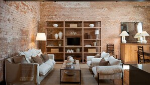 A cozy living room with a brick wall, a wooden bookshelf, a TV, and a dining area with a wooden cabinet and chairs. - The Rox Hobart (Hobart)
