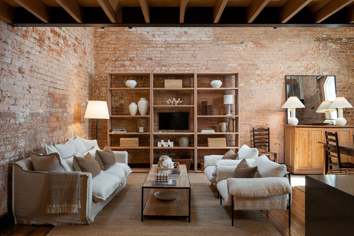 Un salon chaleureux avec un mur en briques, une bibliothèque en bois, un téléviseur et un coin repas comprenant un buffet en bois et des chaises.