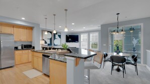 A modern kitchen with wooden cabinets, a central island, and a dining area with a round table and bar stools. - Convenient and Accessible, Park + BBQ + Pool +Gym by Hello Hideout (San Jose)