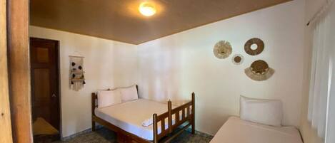 Un dormitorio pequeño y acogedor con cama de madera, una mesita de noche individual y una silla pequeña. Hay una puerta que da a otra habitación y un estante en la pared con objetos decorativos.