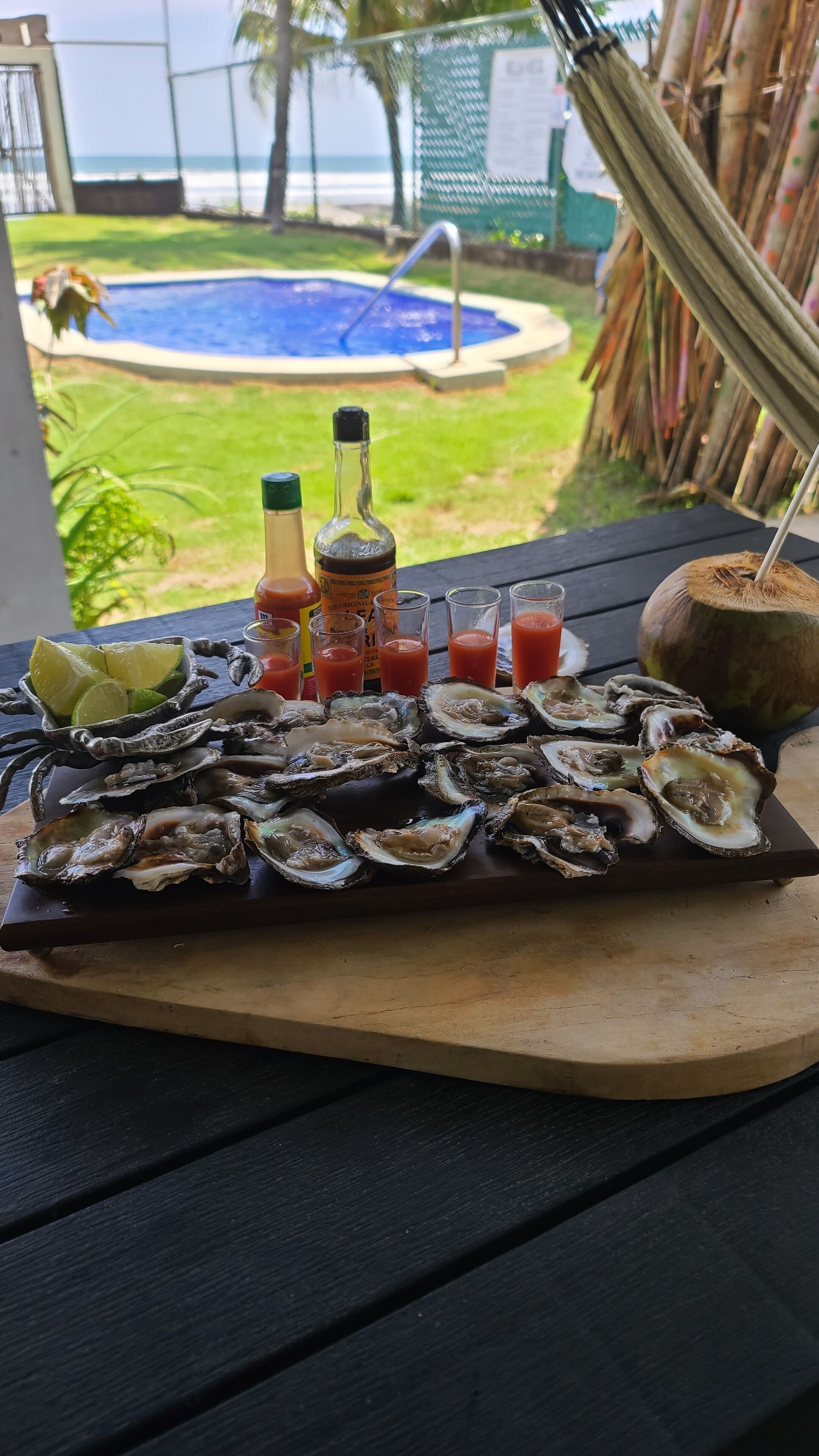 Een houten dienblad met oesters, limoen en diverse sauzen op een tafel.
