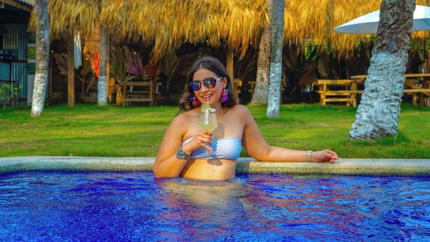 Una persona en una piscina con un entorno tropical, que incluye palmeras y una estructura de techo de paja.