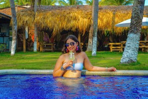 A person in a pool with a tropical setting, including palm trees and a thatched roof structure. - Bella Vista Hotel Boutique y Restaurante (Jucuaran)