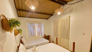 Un dormitorio pequeño y acogedor con dos camas individuales, cabecero de madera, mesita de noche y una cesta colgante con flores.