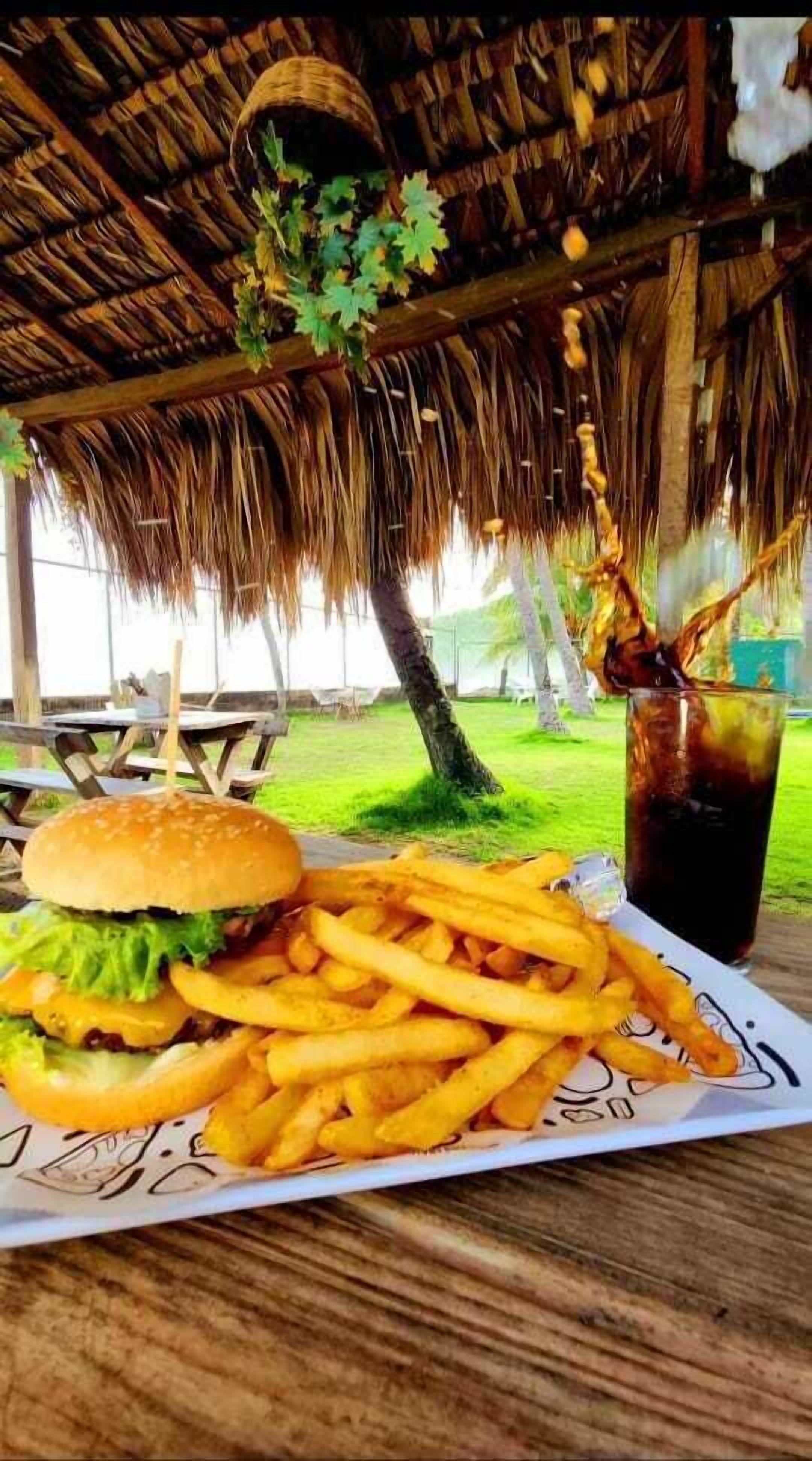 A meal of a burger and fries on a wooden table under a thatched roof.