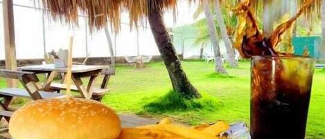 A meal of a burger and fries on a wooden table under a thatched roof.