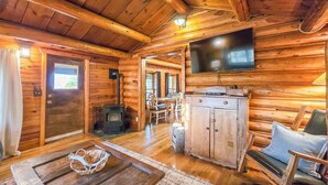 A cozy log cabin interior with a wooden dining table, a sofa, a television mounted on the wall, and a fireplace. - 20 min to Yellowstone, Family Cabin, Fire Pit (Island Park)