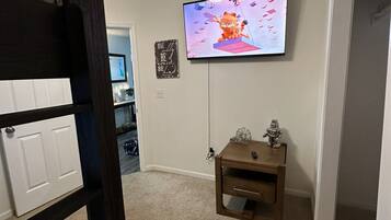A room with a bunk bed, a television mounted on the wall, a small wooden nightstand, and a motivational quote sign.
