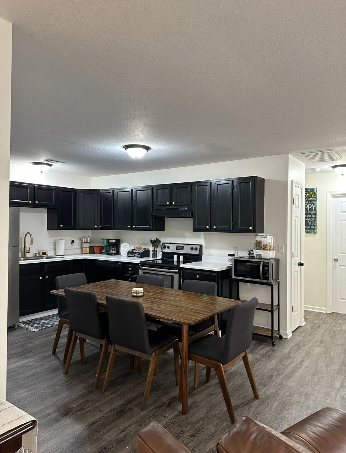 A modern kitchen with dark cabinets, a wooden dining table, and a microwave on a cart.