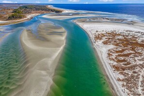 An aerial view of a coastal area with clear water channels, sandy beaches, and a small forested area.