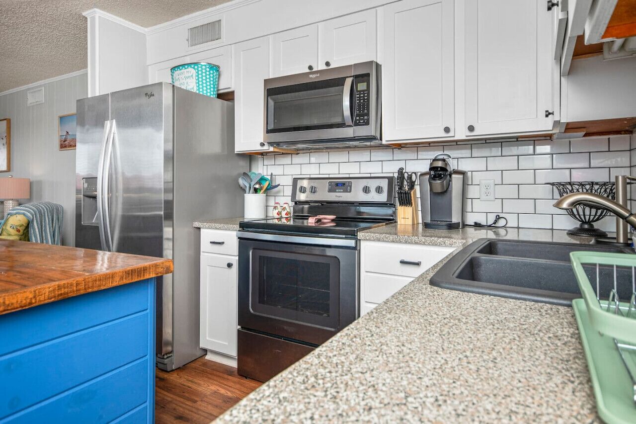 Una cocina compacta con armarios blancos, un refrigerador de acero inoxidable, un microondas, un horno y una encimera de granito.