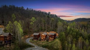 A lodge with multiple wooden cabins surrounded by dense forest, featuring a winding road leading to the cabins.