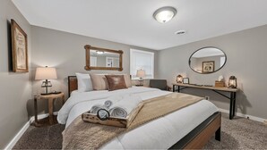 Ein Hotelzimmer mit einem großen Bett, zwei Nachttischen, einem Schreibtisch mit Stuhl, einem runden Spiegel und einer Deckenleuchte.