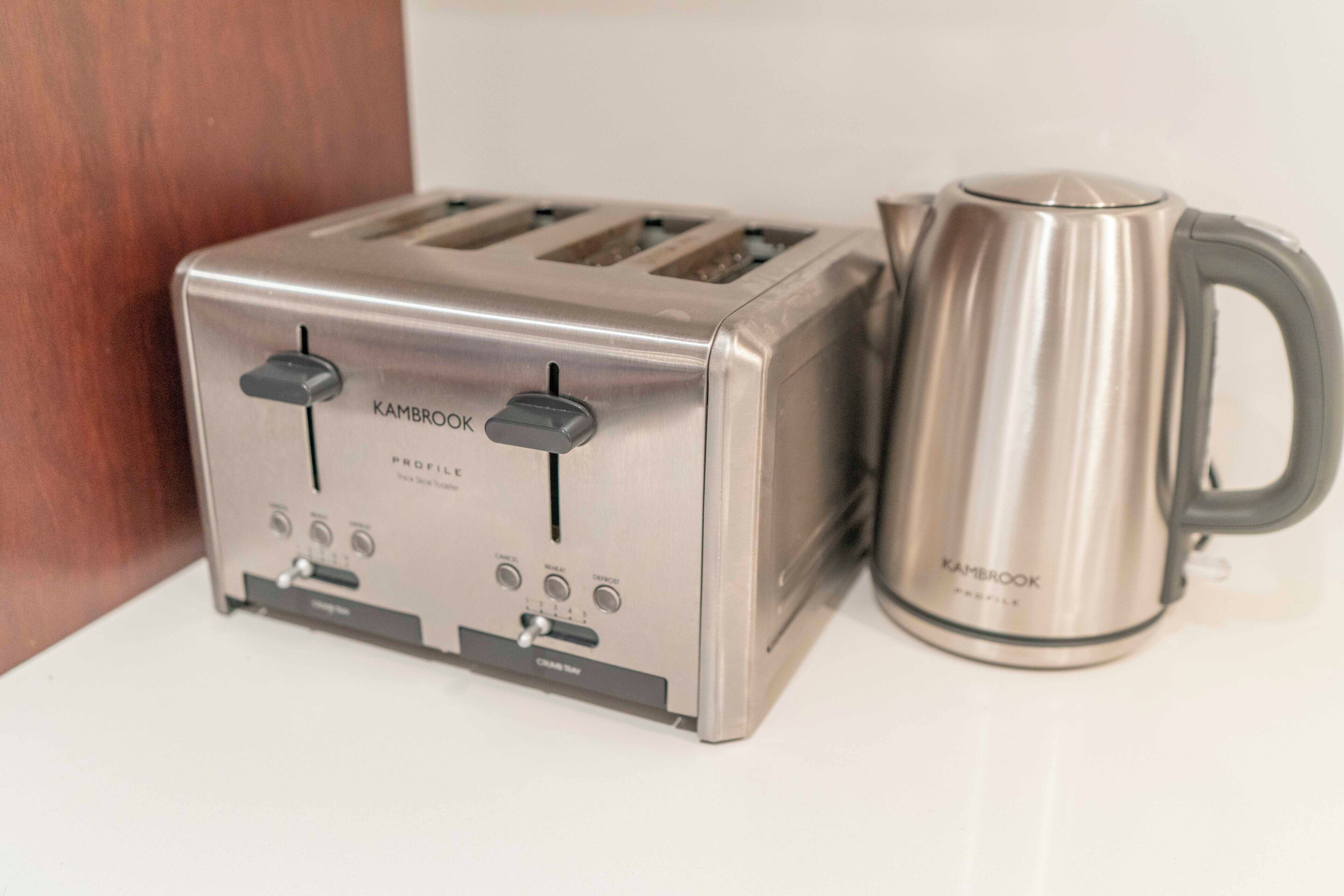 Un grille-pain et une bouilloire en acier inoxydable, tous deux portant la marque « KAMBROOK », sont posés sur une surface blanche.