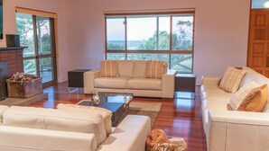A spacious living room with a large window, a fireplace, and a cozy seating area. - The Hideaway by Gatt Wines (Flaxman Valley)