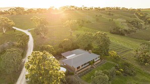 A large, single-story building with a flat roof, surrounded by a well-maintained lawn and a dirt road. - The Hideaway by Gatt Wines (Flaxman Valley)