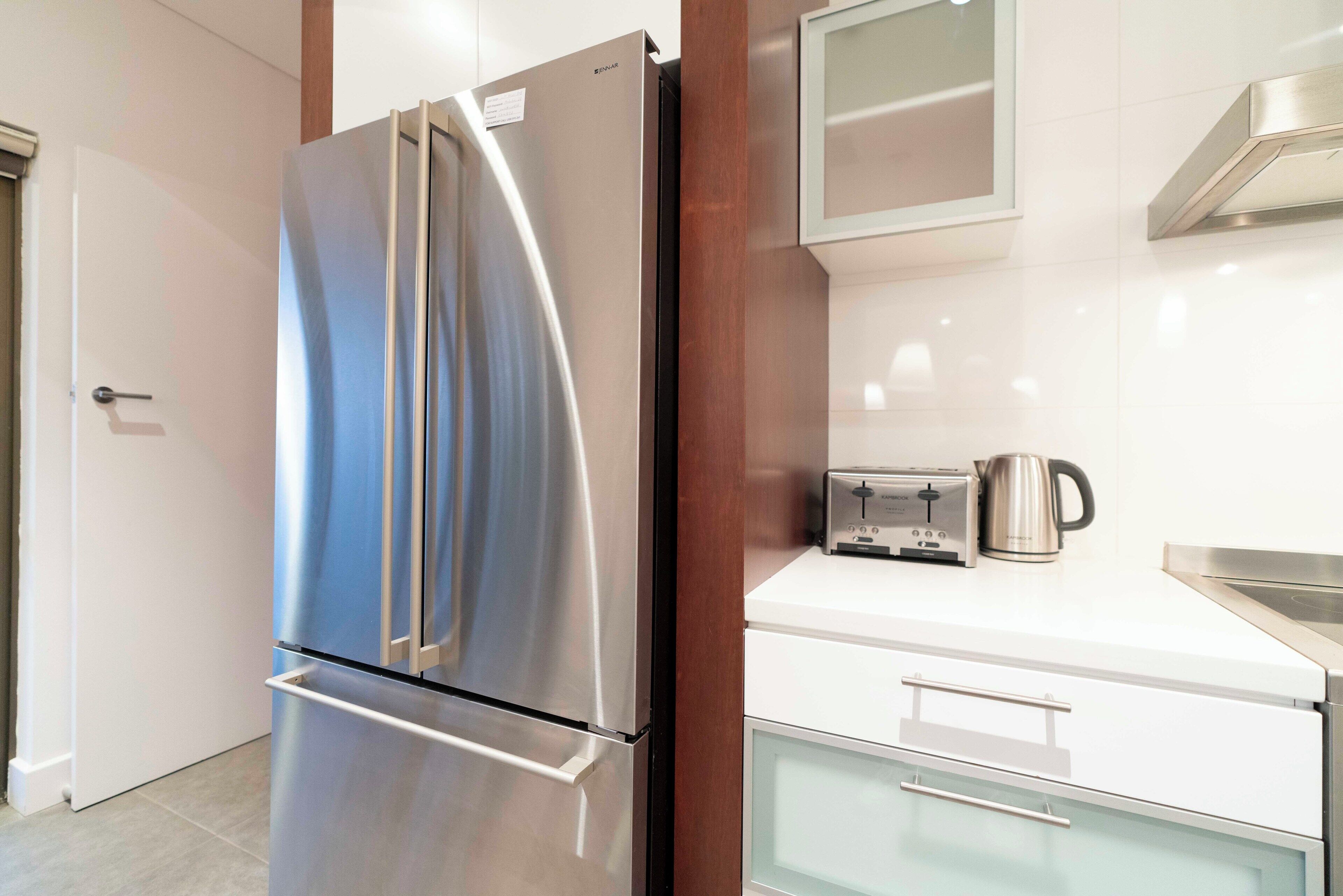 Una cocina moderna con un refrigerador de acero inoxidable, un tostador y una tetera sobre la encimera.