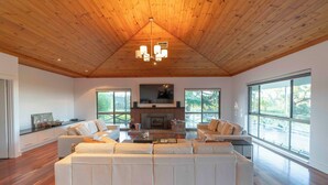 A spacious living room with a large sectional sofa, a fireplace, and large windows offering views of the outdoors. - The Hideaway by Gatt Wines (Flaxman Valley)