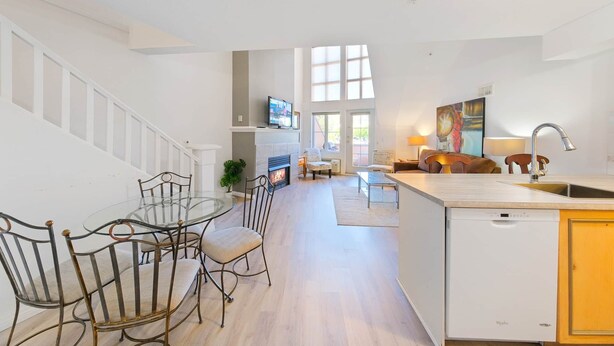 Una cucina moderna con isola centrale, una zona pranzo con tavolo in vetro e una scala che conduce a un piano superiore.