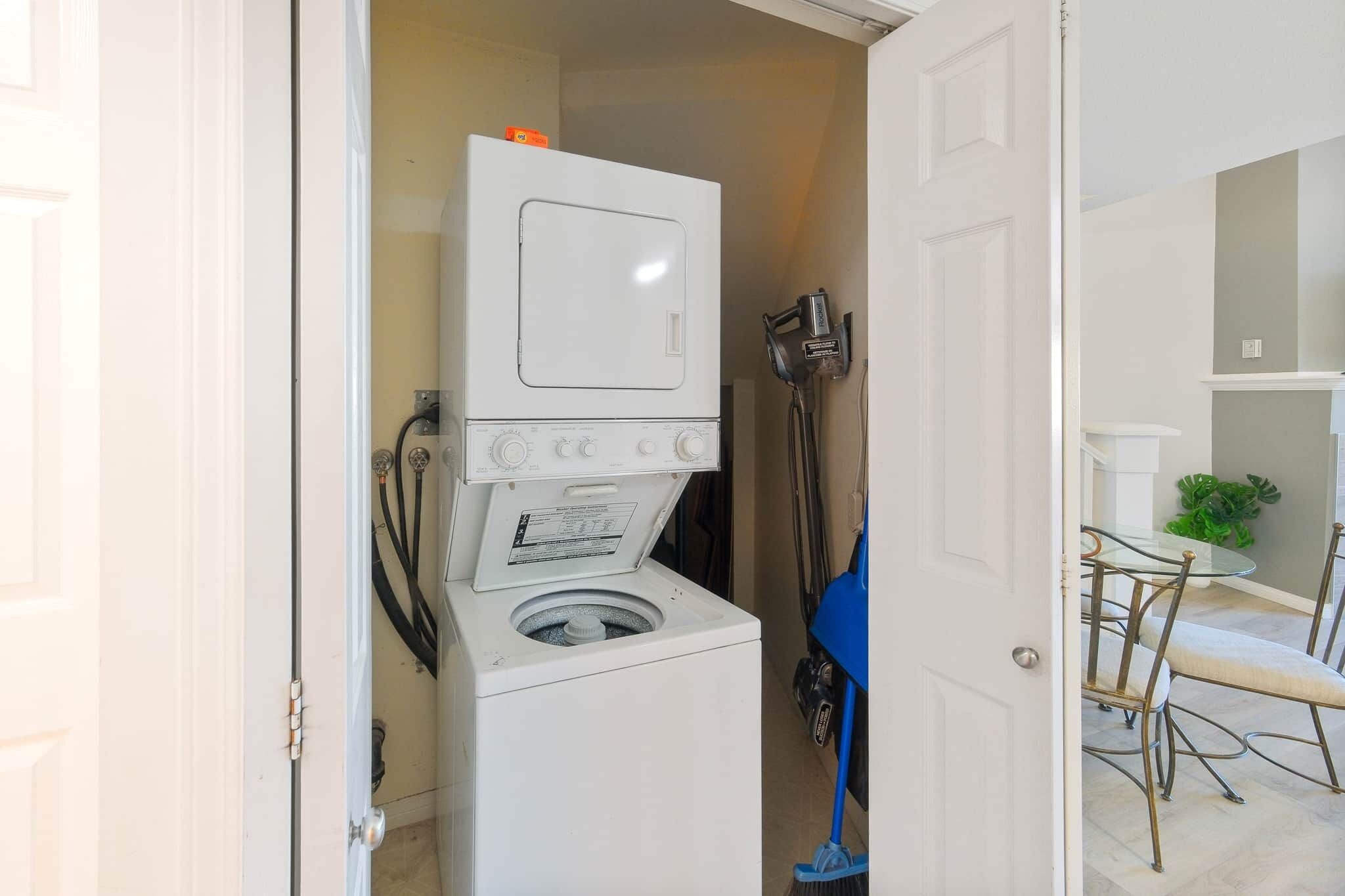 Un espace buanderie avec une machine à laver et un sèche-linge superposés, une serpillière bleue et une table à manger avec des chaises.