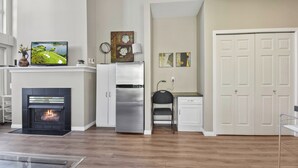 A modern kitchen with a fireplace, stainless steel appliances, and a dining area with a chair and table. - Executive Studio - 314B (Kelowna)