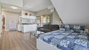 A modern bedroom with a large bed, a sofa, and a kitchenette. - Executive Studio - 314B (Kelowna)