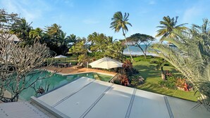 Une piscine dotée d’une terrasse blanche, entourée de palmiers et bordée d’une pelouse.