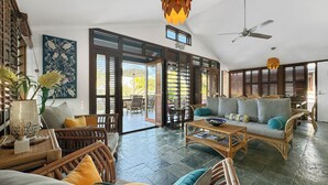 Un vaste espace de vie comprenant un grand canapé, une table basse et des meubles en osier. On y trouve également un ventilateur de plafond et un luminaire décoratif suspendu.