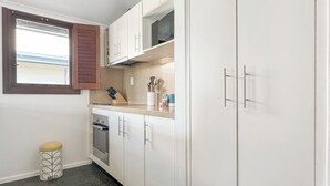Une cuisine avec des meubles blancs, un four à micro-ondes et une fenêtre dotée de volets en bois.