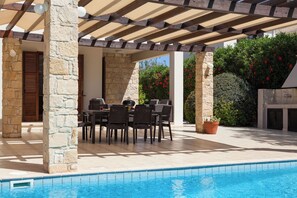 An outdoor pool area with a covered patio, stone pillars, and a table with chairs. - Luxurious Villa Retreat with Panoramic Views (Paphos)