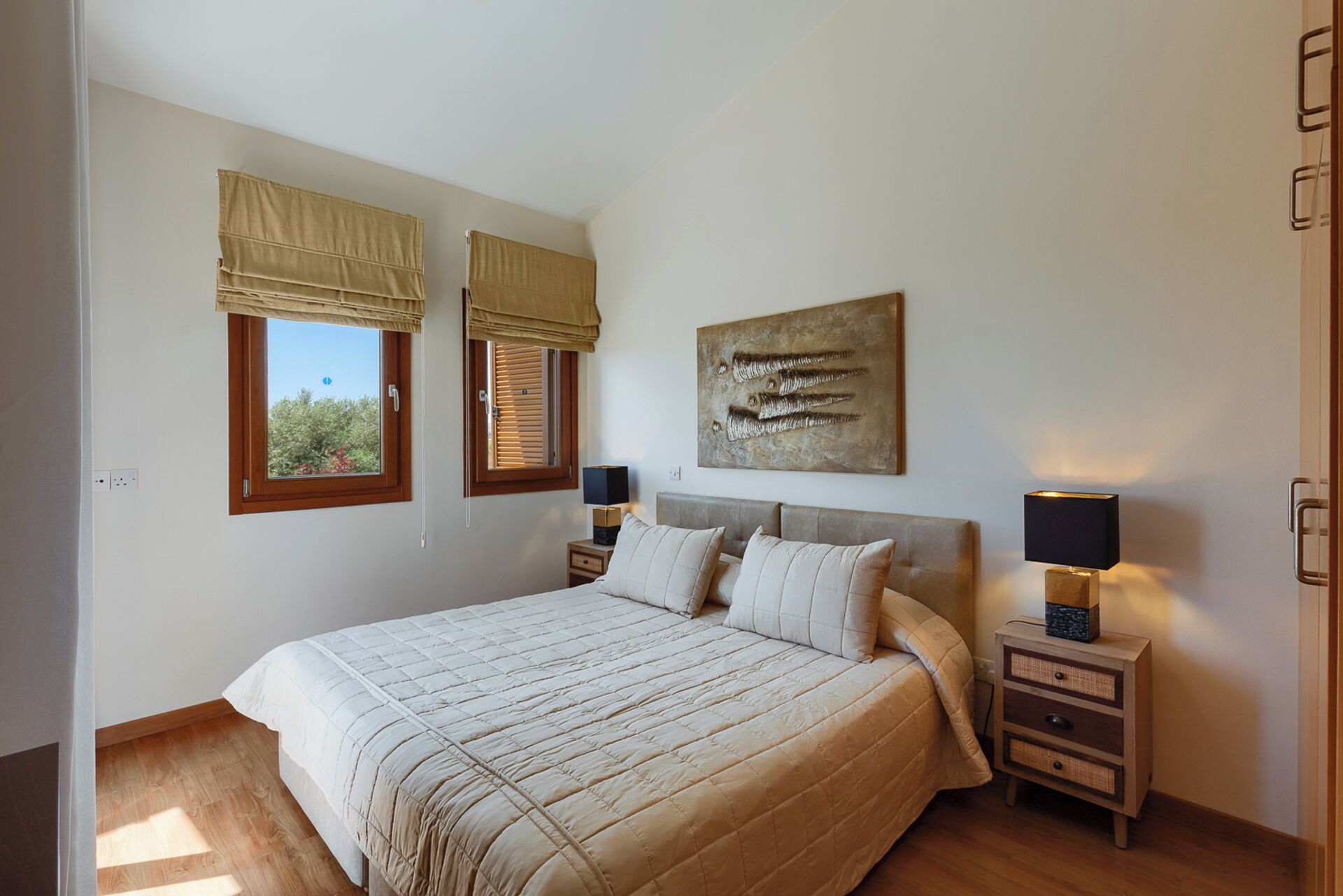 Un dormitorio con una cama grande, dos mesitas de noche con lámparas, una ventana con vistas y una obra de arte colgada en la pared.