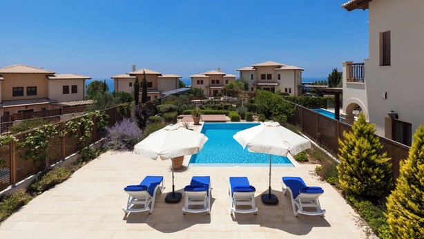 A pool area with lounge chairs and umbrellas, surrounded by buildings with a Mediterranean architectural style. - Luxury Villa Retreat with Unmatched Elegance and Serenity (Paphos)