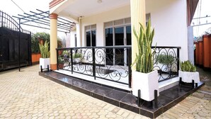 Un espacio al aire libre techado con piso de baldosas, baranda de metal negro y plantas en macetas.