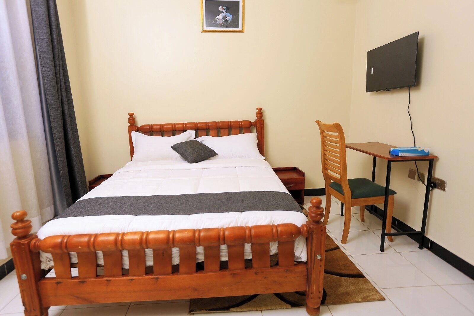 A neatly made bed with a wooden headboard, a desk with a chair, and a television on the wall.