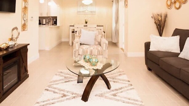 Un salon avec une table basse en verre, un canapé et, au fond, un coin repas.