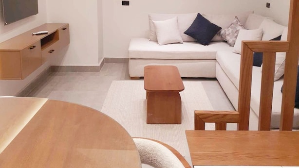 Ein modernes Wohnzimmer mit einer Couch, einem Couchtisch, einem an der Wand montierten Fernseher und einem Holzesstisch.
