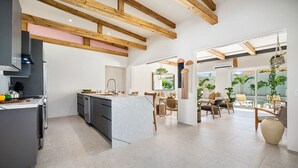 A modern kitchen with a marble island, wooden beams, and a dining area with a view of the outdoors. - NEW 6BR Playground Private Pool Pro-BBQ Palapa (Noord)