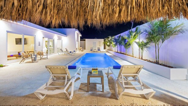 A poolside area with lounge chairs, a table, and a thatched roof overhead. - NEW 6BR Playground Private Pool Pro-BBQ Palapa (Noord)