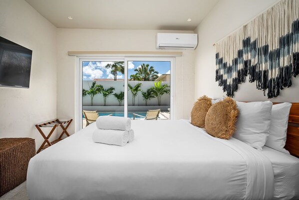 Habitación de hotel con cama, vistas a palmeras y una piscina, y un tapiz grande tejido en la pared.