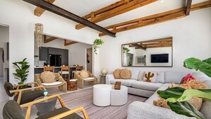 A modern living room with a grey sofa, wooden chairs, and a dining area with a kitchen in the background. - NEW 6BR Playground Private Pool Pro-BBQ Palapa (Noord)