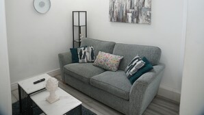 Ein Wohnzimmer mit grauem Sofa, einem weißen Couchtisch, einer Fernbedienung und einer dekorativen Skulptur.