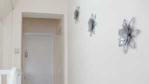 Ein Korridor mit Holzboden, weißen Wänden und einer weißen Tür am Ende. Drei metallische Wanddekorationen sind angebracht.