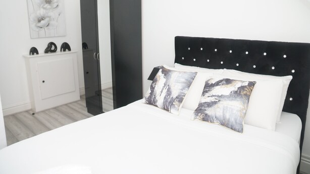 Ein Schlafzimmer mit schwarzem Kopfteil, weißer Bettwäsche und zwei Kissen mit einem Naturmotiv.