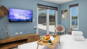 Une chambre moderne équipée d’une télévision, d’un plateau en bois avec des fruits, d’un ventilateur et d’un lit avec des serviettes.