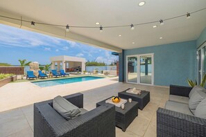 Ein überdachter Außenbereich mit Pool, Liegestühlen und Gartenmöbeln.