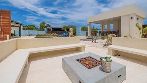 Une terrasse extérieure moderne, dotée d’un foyer, d’espaces pour s’asseoir et d’un coin salon au bord de la piscine.